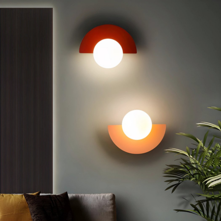 Due applique a mezzaluna in stile retrò, di colore rosso e rosa, sono appese a una parete accanto a una pianta d'appartamento