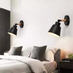 una camera da letto presenta un letto con cuscini grigi e due applique nere su una parete bianca